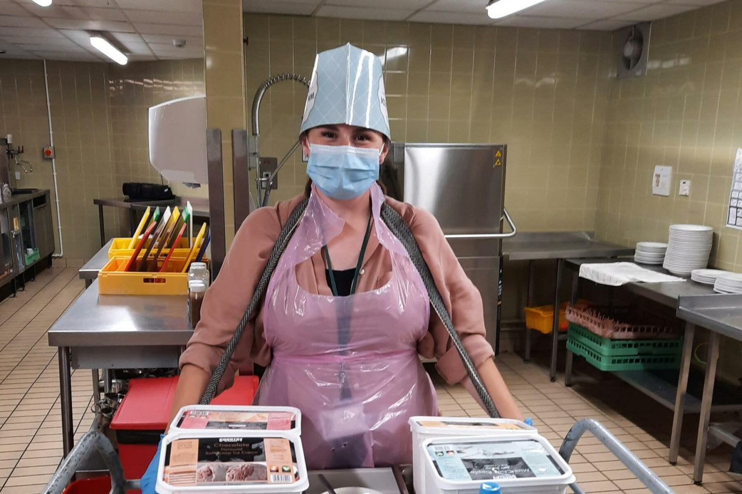 Hannah in a commercial kitchen wearing PPE behind a trolley with ice cream on