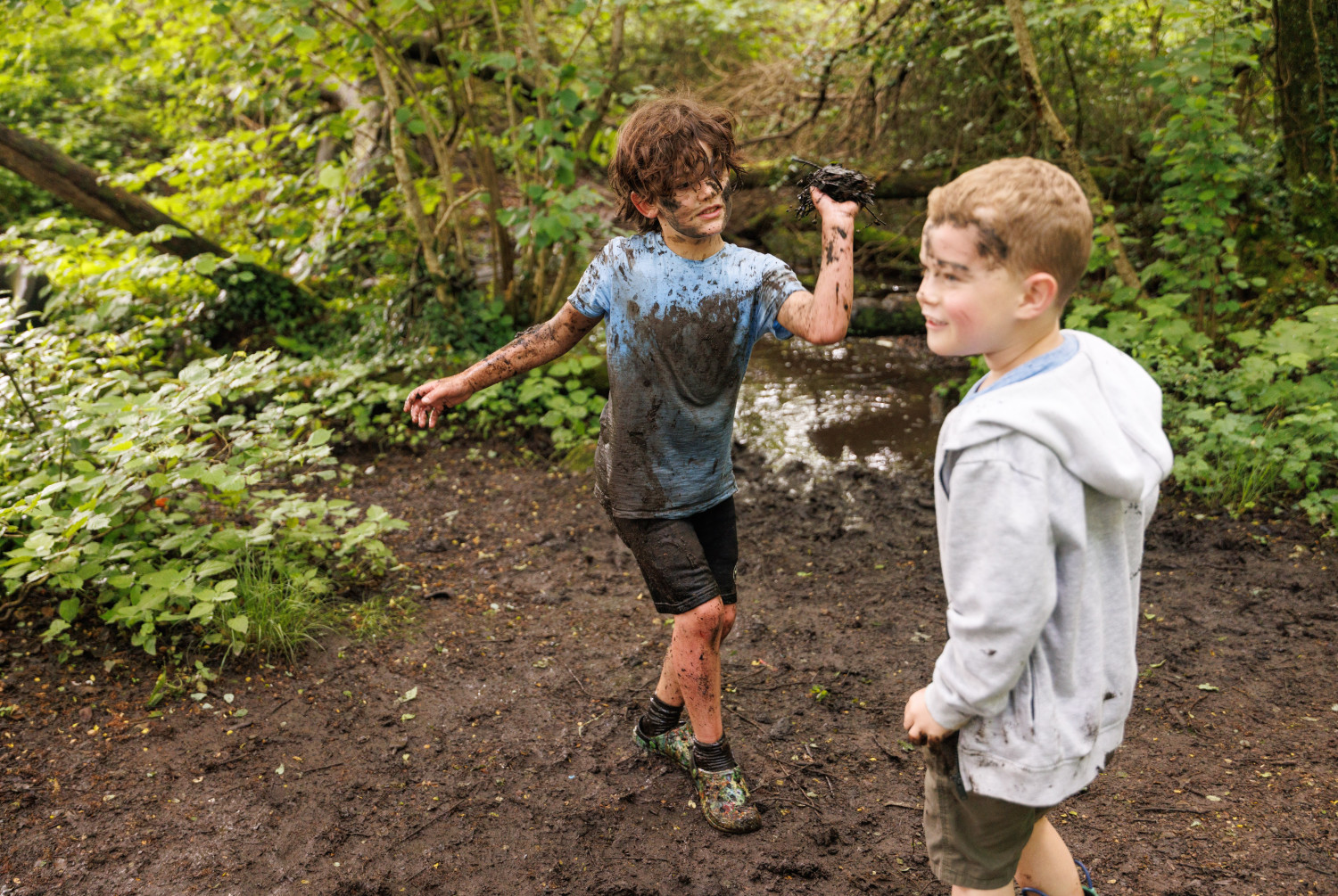 Two young boys playing in the mud