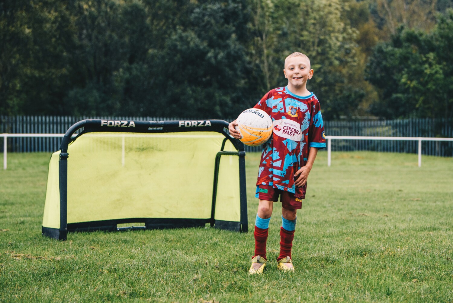 A young boy with a football stood next to a goal post